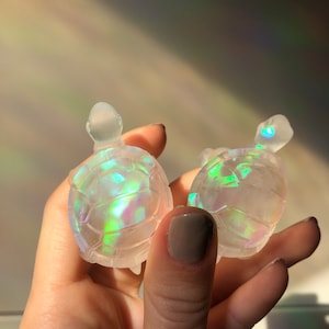 May include: Two iridescent clear glass turtle figurines. The turtles are small and have a detailed shell design.