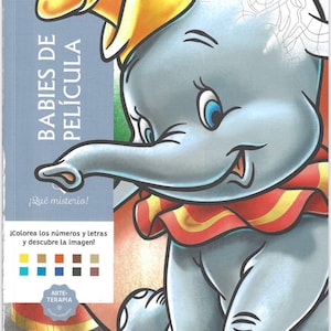 May include: A Disney coloring book cover featuring Dumbo the elephant wearing a yellow hat and a red and yellow ruffled collar. The cover includes the text BABIES DE PEL&Iacute;CULA, &iexcl;Qu&eacute; misterio!, &iexcl;Colorea los n&uacute;meros y letras y descubre la imagen!, ARTE-TERAPIA, and hachette HEROES, along with a color palette guide.