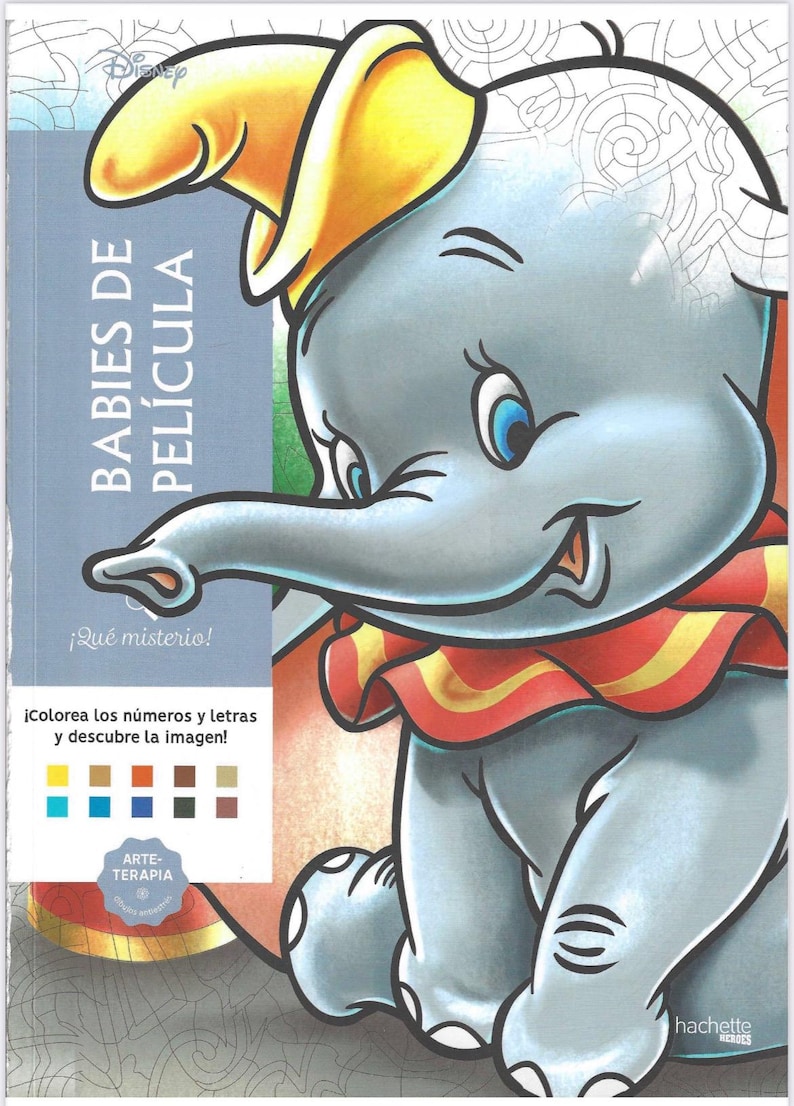 May include: A Disney coloring book cover featuring Dumbo the elephant wearing a yellow hat and a red and yellow ruffled collar. The cover includes the text BABIES DE PEL&Iacute;CULA, &iexcl;Qu&eacute; misterio!, &iexcl;Colorea los n&uacute;meros y letras y descubre la imagen!, ARTE-TERAPIA, and hachette HEROES, along with a color palette guide.