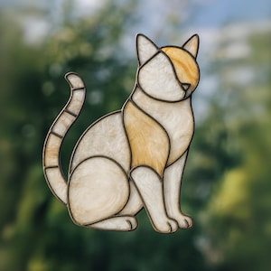 Op de afbeelding: Gebrandschilderde kattenfiguur in zittende positie. De kat heeft een crème- en amberkleurenschema met donkerbruine contouren. Het ontwerp doet denken aan een mozaïek of een glas-in-loodraam, met een gedetailleerde weergave van de kattenkenmerken.