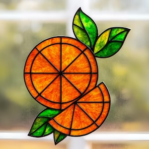 May include: A stained glass orange slice design with a black outline. The orange fruit is a vibrant orange color, with green and yellow leaves. The design is likely a window cling or suncatcher.
