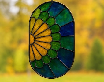 May include: Oval stained glass window panel with a sunburst design. The panel features a sunburst pattern in yellow, green, and blue hues, framed by a dark metal border. The glass is segmented into various shapes, creating a decorative piece.