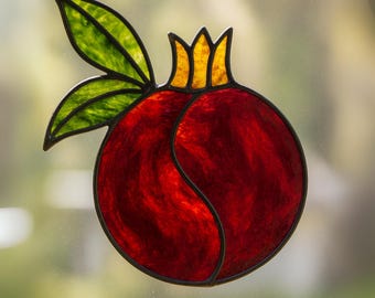 May include: A stained glass pomegranate with a vibrant red body, yellow crown, and green leaves. The fruit is outlined in black, creating a striking contrast. This decorative piece is ideal for adding a touch of color and artistry to any space.