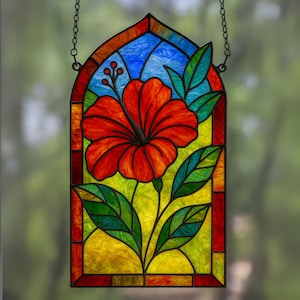 Puede incluir: Panel de ventana de vidriera con una vibrante flor de hibisco roja con hojas verdes y un fondo amarillo y azul. El panel está enmarcado en un color oscuro y cuelga de una cadena. Una pieza decorativa para una ventana o pared.