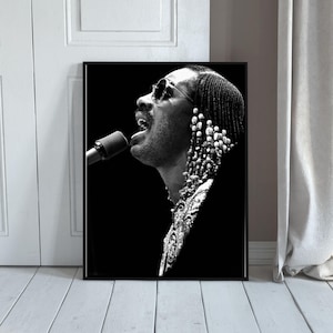 Puede incluir: Impresión enmarcada en blanco y negro de un cantante con gafas de sol y un micrófono. El cantante lleva joyas de cuentas y tiene el pelo trenzado. La imagen es un retrato del cantante cantando.