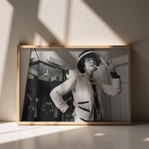 Peut inclure: Photographie encadrée en noir et blanc d'une femme portant un chapeau, un blazer et des perles, tenant une cigarette. L'image est dans un cadre en bois, avec un mur clair et des ombres en arrière-plan.