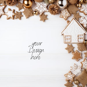 Pu&ograve; includere: Una composizione festosa di decorazioni natalizie su una superficie di legno bianco. L'esposizione comprende biscotti di pan di zenzero, ornamenti dorati, pigne e decorazioni a forma di stella. Il testo "your Design here" &egrave; scritto in corsivo.