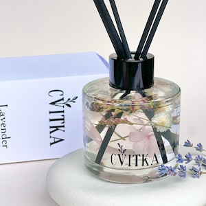 Könnte beinhalten: Ein Diffusor aus klarem Glas mit schwarzem Deckel und schwarzen Stäbchen. Die Flasche ist mit einer klaren Flüssigkeit gefüllt und enthält getrocknete Blumen und Blütenblätter. Die Flasche trägt ein Etikett mit der Aufschrift "CVITKA" und "Lavendel".