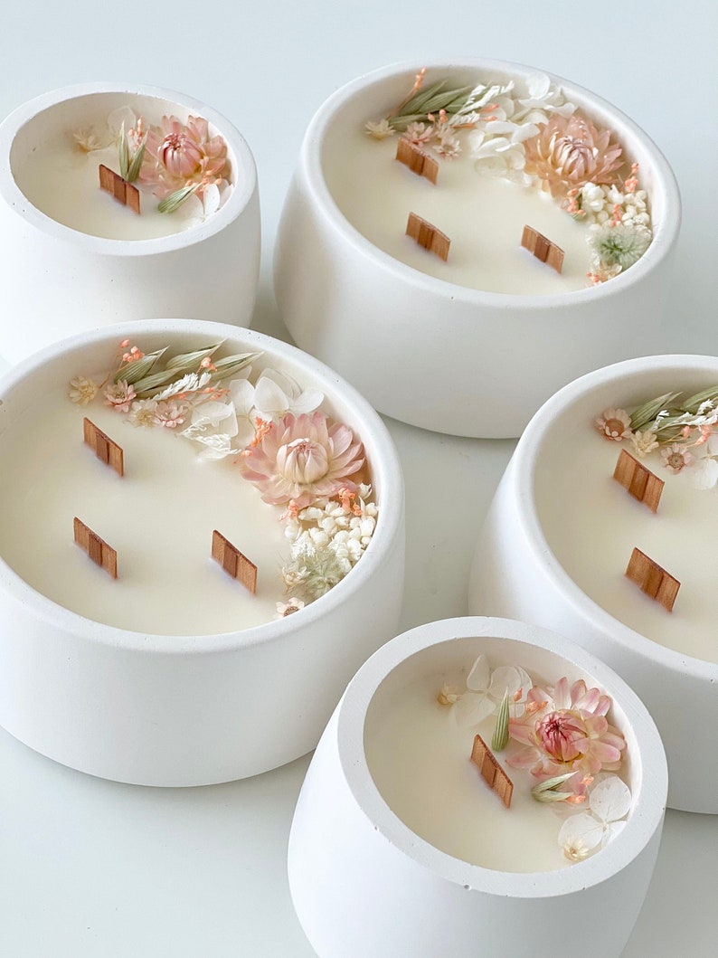 May include: Four white ceramic candle holders with a variety of dried flowers and greenery embedded in the wax. Each candle has two wooden wicks.