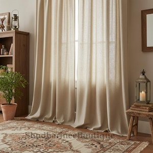 Puede incluir: Cortinas de lino beige cuelgan frente a una ventana, con pliegues suaves. Un armario de madera, una planta en maceta y una alfombra estampada están en primer plano. Un pequeño taburete de madera sostiene una linterna con una vela encendida.