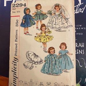 May include: A vintage Simplicity doll pattern, size 10 1/2, with illustrations of dolls in different outfits, such as a hooded cape, a gingham dress, a wedding dress, and a blue gown. The pattern number is 2294, and the price is 35c.