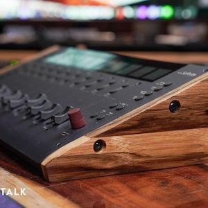 Könnte beinhalten: Ein schwarzes Audio-Mischpult mit einem Holzständer. Das Pult verfügt über mehrere Knöpfe, Tasten und einen Bildschirm. Der Ständer ist aus dunklem Holz mit natürlicher Maserung.