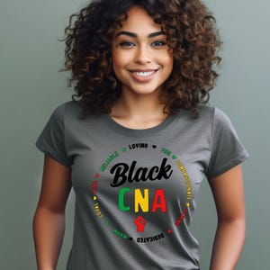 May include: A grey crew neck t-shirt with the words "Black CNA" in a circular design. The design includes a raised fist and words like "reliable" and "loving".