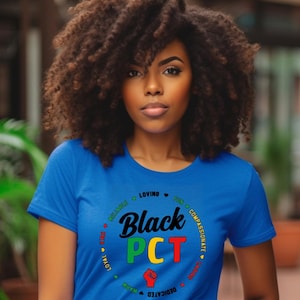 May include: A woman wearing a blue t-shirt with the words "Black PCT" in a circular design. The design includes a raised fist and words like "loving" and "compassionate".