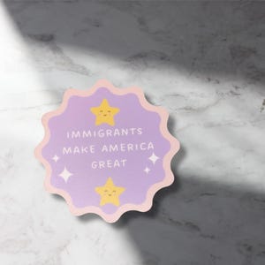 以下が含まれることがあります： 「IMMIGRANTS MAKE AMERICA GREAT」の文字が入った、スカラップエッジの薄紫色のステッカー。2つの黄色の笑顔の星と4つの白いダイヤモンドの形が特徴です。