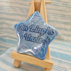 May include: A blue star-shaped button with a glittery finish. The button says "Jin Ling's Uncle" in a white, cursive font.
