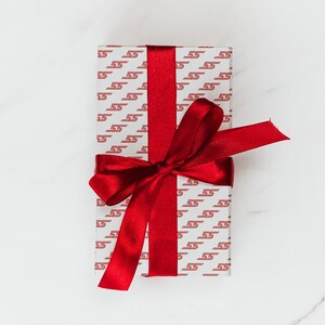 May include: A white gift box with a red ribbon and bow. The box is wrapped in paper with a repeating pattern of the number "55" in red.