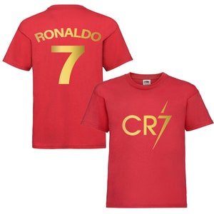 Pode incluir: Camiseta vermelha com letras douradas nas costas que diz "RONALDO 7" e um design de raio dourado na frente que diz "CR7".