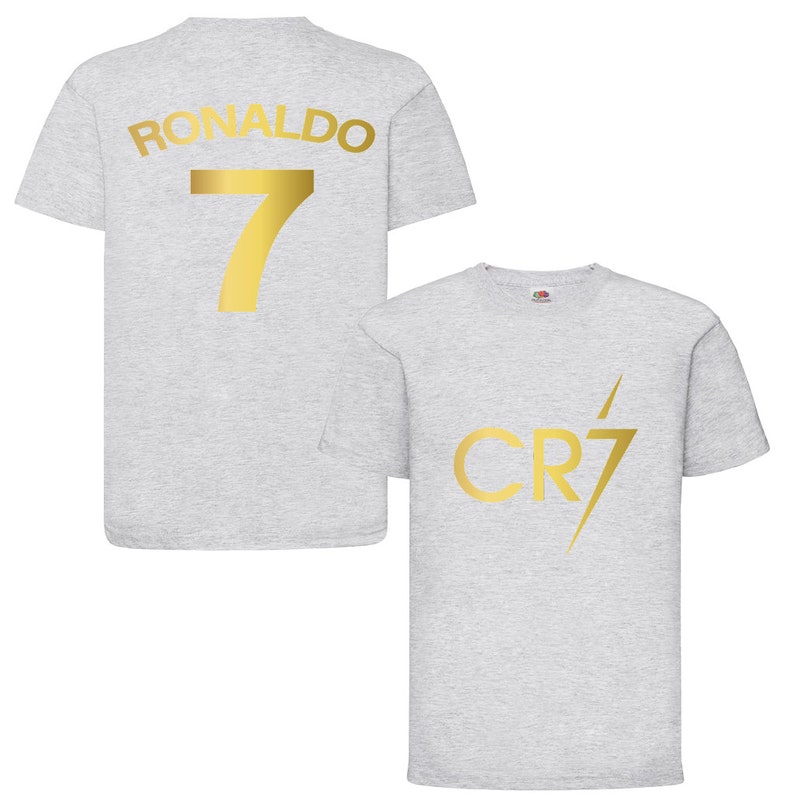 Pode incluir: Duas camisas cinzas com letras douradas. Uma camisa tem "RONALDO 7" nas costas. A outra camisa tem "CR7" com um raio.