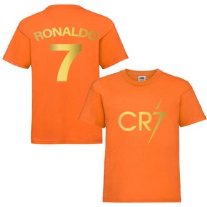 Pode incluir: Camiseta laranja com letras douradas. A parte de tr&aacute;s da camiseta diz "RONALDO 7". A parte da frente da camiseta diz "CR7" com um raio.