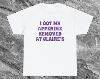 Puede incluir: Camiseta blanca con texto morado que dice "Me quitaron el apéndice en Claire's".