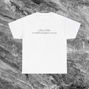 May include: White t-shirt with the text "6 feet of dirt would look great on you" in a simple, sans-serif font. The shirt has a crew neck and short sleeves. The text is centered on the front of the shirt.