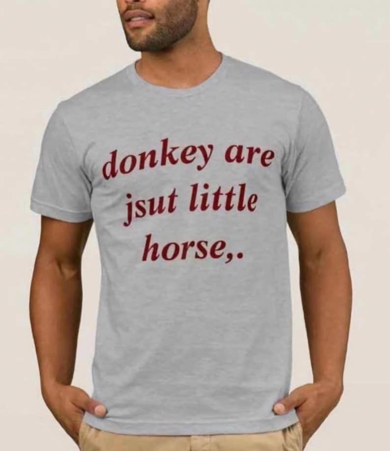 Op de afbeelding: Lichtgrijs t-shirt met de tekst "donkey are jsut little horse,.." in bordeauxrood. Het shirt met korte mouwen lijkt van een zacht materiaal te zijn.
