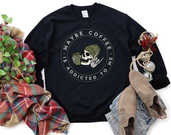 May include: Black sweatshirt with a white graphic of a skeleton holding a coffee cup. The graphic says "Maybe coffee is addicted to me".