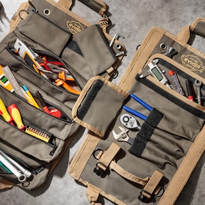 May include: Two canvas tool rolls with multiple pockets and compartments. The rolls are filled with various tools, including screwdrivers, pliers, wrenches, and a level. The rolls are labeled "The Ryker Collection".