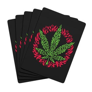 Può includere: Un set di carte da gioco nere con un design a foglia di cannabis verde e rossa. La foglia è dettagliata con un motivo decorativo e circondata da un bordo rosso a forma di fiamma. Le carte sono a ventaglio, mostrando il design.