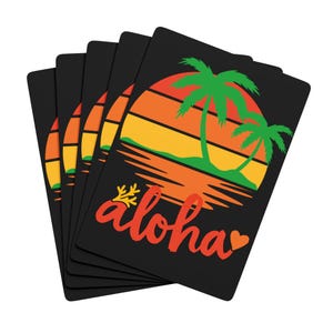 May include: A set of black playing cards with a tropical sunset design. The cards feature palm trees and the word "aloha" in red script. The design uses orange, yellow, and green colours.