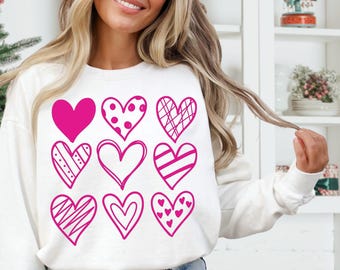 May include: White sweatshirt with a pink design of nine different hearts. The hearts are all different shapes and sizes and have different patterns.