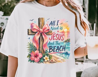 May include: A white t-shirt featuring a graphic print of a wooden cross adorned with a large pink bow, tropical hibiscus flowers, and a beach sunset scene. The text reads, All I Need is JESUS And The BEACH, in a mix of blue and pink script and block lettering.