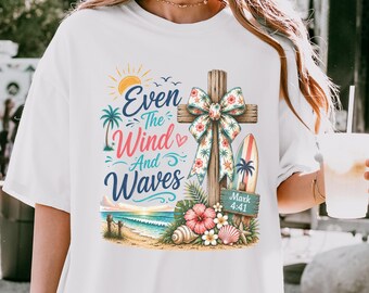 May include: A white t-shirt featuring a graphic print of a wooden cross with a floral bow, a surfboard, palm trees, seashells, and hibiscus flowers. The text reads Even The Wind And Waves and Mark 4:41, set against a beach and ocean scene.