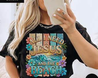 May include: Black t-shirt with a colorful graphic that reads "All I Need Is Jesus And The Beach." The design features a beach scene with waves, palm trees, and flowers. The shirt is labeled "Comfort Colors" and "Black."