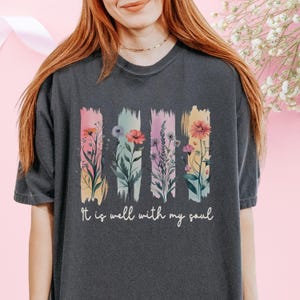 May include: A dark gray t-shirt with a floral design and the text "It is well with my soul".