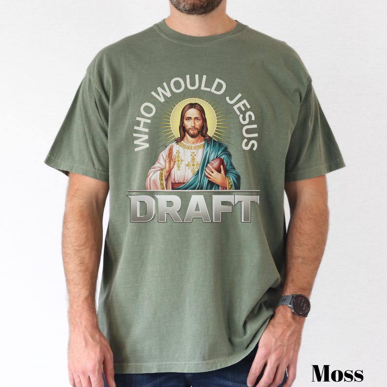 Puede incluir: Una camiseta verde con el texto "Who Would Jesus Draft" en un c&iacute;rculo alrededor de una imagen de Jes&uacute;s sosteniendo un bal&oacute;n de f&uacute;tbol.