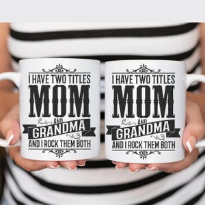 Puede incluir: Dos tazas de caf&eacute; blancas con texto negro que dice "Tengo dos t&iacute;tulos Mam&aacute; y Abuela y las rockeo a ambas".