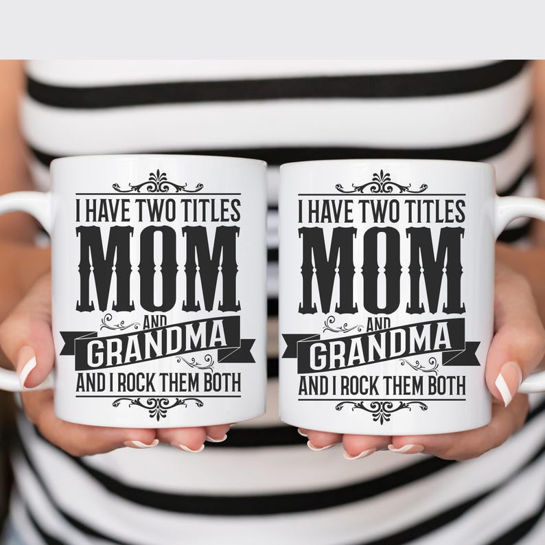 Puede incluir: Dos tazas de caf&eacute; blancas con texto negro que dice "Tengo dos t&iacute;tulos Mam&aacute; y Abuela y las rockeo a ambas".