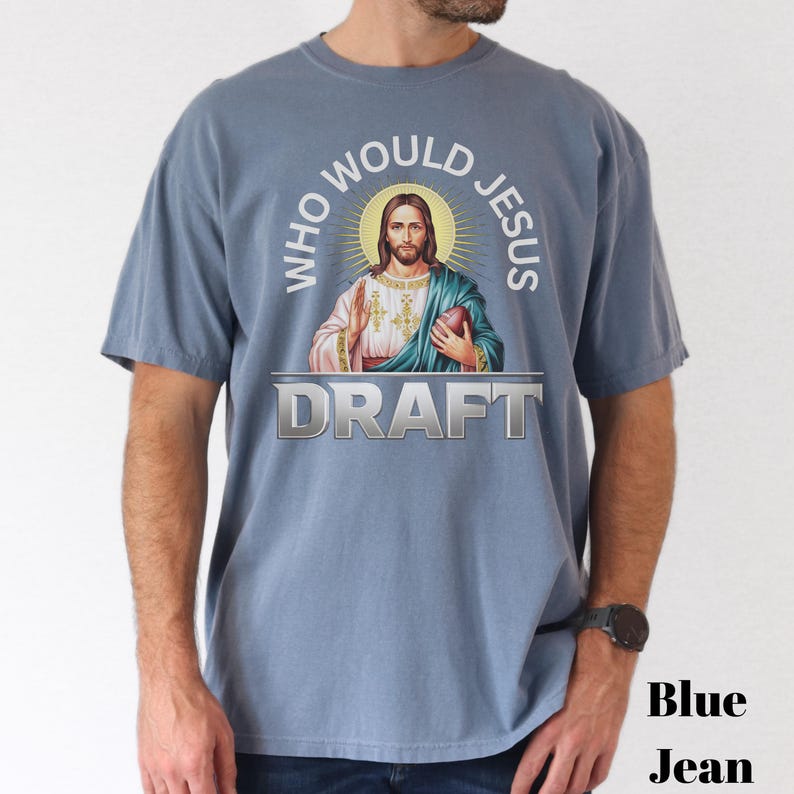 Puede incluir: Una camiseta azul con un gr&aacute;fico de Jes&uacute;s sosteniendo un bal&oacute;n de f&uacute;tbol y el texto "Who Would Jesus Draft".