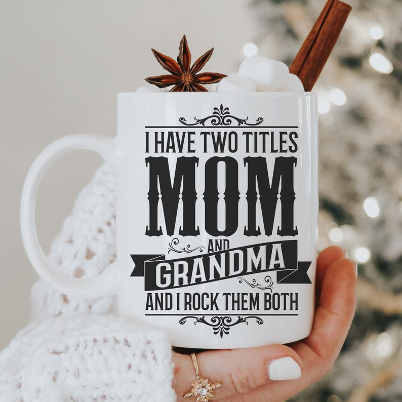 Puede incluir: Taza de cer&aacute;mica blanca con un dise&ntilde;o negro que dice "Tengo dos t&iacute;tulos Mam&aacute; y Abuela y los rockeo ambos".