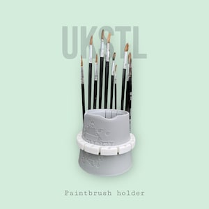 Könnte beinhalten: Ein grauer Pinselhalter mit einem runden Sockel und einem zylindrischen Oberteil. Der Halter hat eine strukturierte Oberfläche mit einem Weltkartenmuster. Der Halter ist mit verschiedenen Pinseln gefüllt.