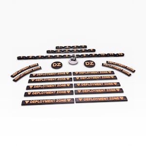 May include: A set of black and orange game components, featuring numbered markers, deployment zone indicators, and DZ tokens. The pieces are laid out on a white surface, likely for a tabletop game.