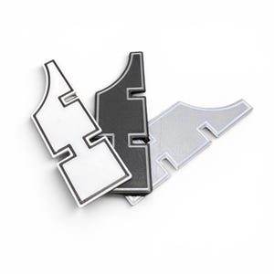 May include: Three abstract, stylized shapes in white, black, and silver. Each has a unique, geometric design with a curved top and a rectangular base. The shapes are arranged on a white background.