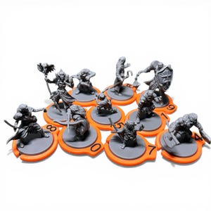 Puede incluir: Un conjunto de figuras de fantasía en miniatura grises sobre bases naranjas y grises. Cada figura está diseñada de forma única, representando varios personajes con armas y armaduras. Las bases están numeradas del 0 al 9.