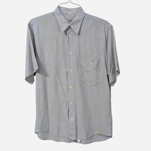 May include: A light gray short-sleeved button-down shirt with a chest pocket. The shirt is hanging on a metal hanger. The fabric has a subtle pattern.