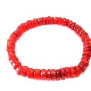 Puede incluir: Una pulsera roja vibrante compuesta por pequeñas cuentas cuadradas. Las cuentas están ensartadas para formar una forma circular, adecuada para la muñeca. La pulsera se presenta sobre un fondo blanco liso.