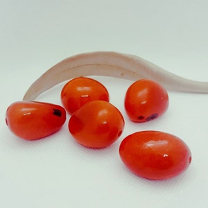 Peut inclure: Cinq perles lisses de forme ovale, de couleur orange vif. Les perles sont brillantes et ont un léger éclat.