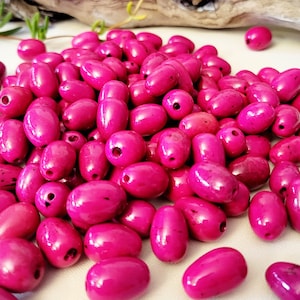 Könnte beinhalten: Ein großer Haufen leuchtend rosa ovaler Perlen. Die Perlen sind aus Holz und haben eine glänzende Oberfläche.