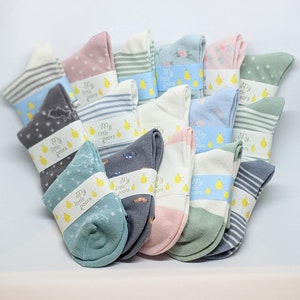 Può includere: Una collezione di 12 paia di calzini per neonati in vari colori e motivi. I calzini sono confezionati con un'etichetta che recita "My Little Pears".